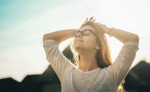 Woman standing outside with the sun at her back and eyes closed taking in the moment.