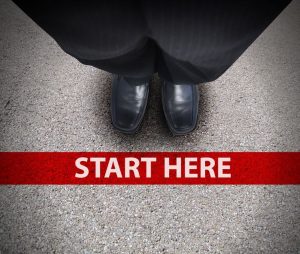 a business man is looking down at his feet with a red race line that says start here to represent a journey